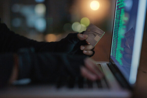 Shot of an unrecognisable hacker using a laptop to hack into a credit account.