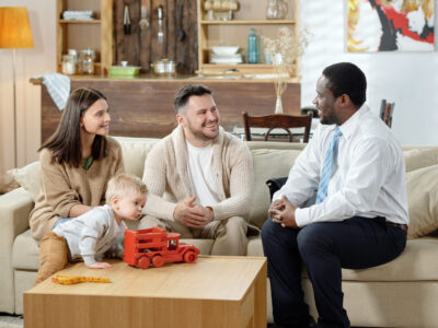 Cheerful counselor and family gathering on couch Diverse man and happy family with boy having real estate consultation sitting together on sofa